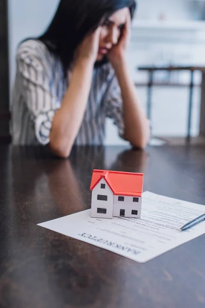 Selektiver Fokus der aufgebrachten Frau am Tisch mit Hausmodell und Stift auf Papier mit Konkursaufschrift — Stockfoto