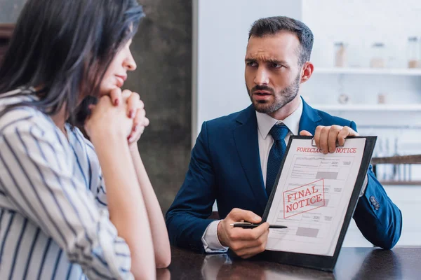 Collectionneur de temps pointant vers les documents avec forclusion et avis final lettrage et regardant femme avec les mains serrées à la table — Photo de stock