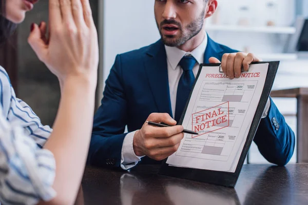 Cropped view of woman and collector pointing with pen at documents with foreclosure and final notice lettering at table — Stock Photo