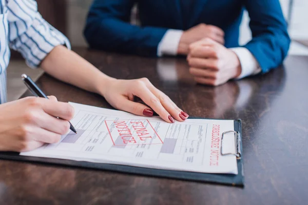 Cropped view of woman writing in documents with foreclosure and final notice near collector at table — Stock Photo