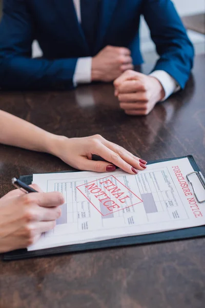 Partial view of woman writing in documents with foreclosure and final notice near collector at table — Stock Photo