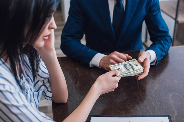 Donna che dà banconote in dollari al collezionista a tavola nella stanza — Foto stock