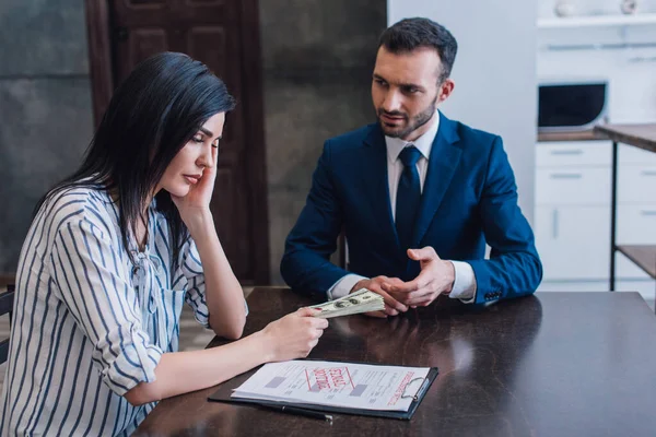 Woman giving dollar banknotes to collector at table with documents and pen in room — Stock Photo