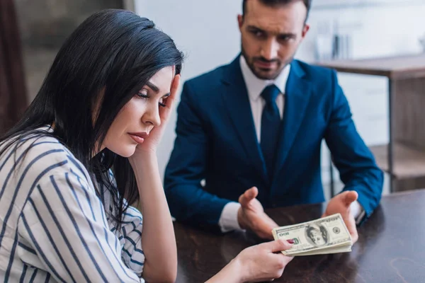 Foco seletivo da mulher chateada dando notas de dólar ao colecionador na mesa no quarto — Fotografia de Stock