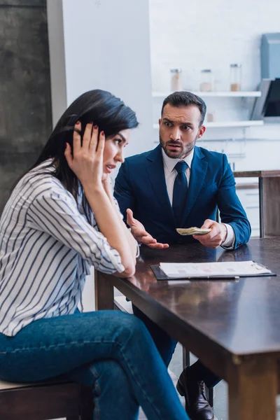 Tense collector with money looking at woman at table in room — Stock Photo