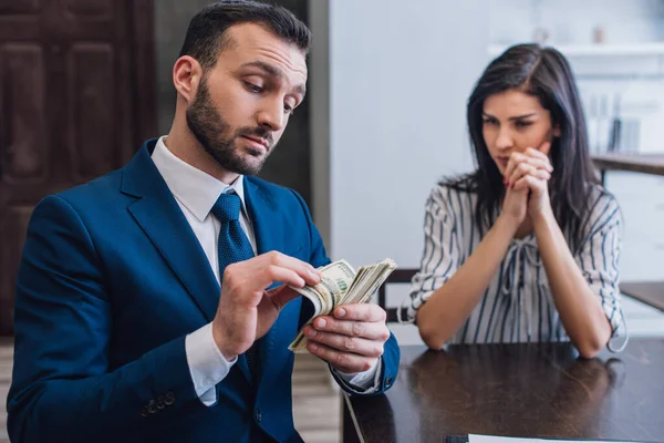 Mulher com as mãos apertadas olhando para coletor contando dinheiro na mesa no quarto — Fotografia de Stock