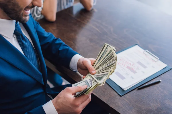 Vue recadrée du collectionneur tenant des billets en dollars près d'une femme à table avec stylo et documents — Photo de stock