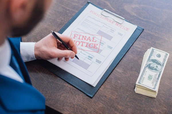 Cropped view of collector writing in documents with foreclosure and final notice lettering near dollar banknotes at table in room — Stock Photo