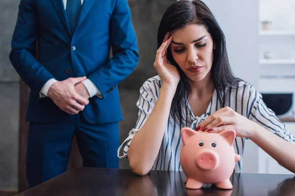 Femme bouleversée touchant tirelire à table près du collectionneur avec les mains serrées — Photo de stock