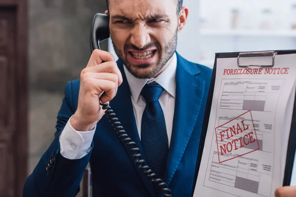 Angry collector with handset and documents with foreclosure and final notice lettering in room — Stock Photo