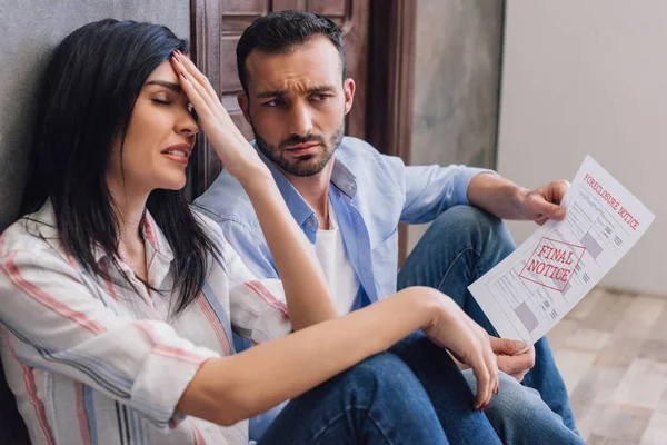 Mulher estressada com marido segurando documento com encerramento e aviso final lettering no chão no quarto — Fotografia de Stock