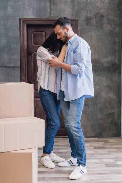 Hombre abrazando molesto esposa cerca de cajas en la habitación - foto de stock