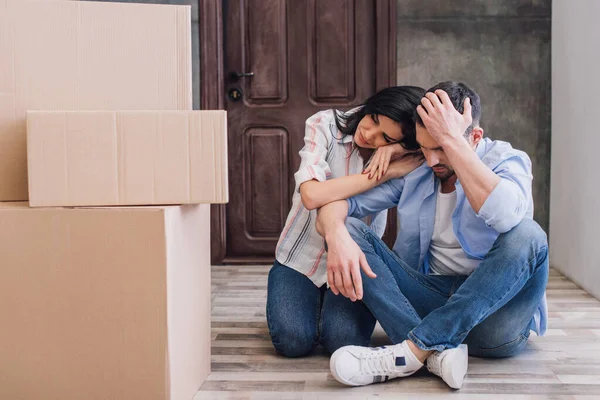 Empörte Frau lehnt sich mit überkreuzten Beinen an Mann in der Nähe von Boxen auf dem Boden — Stockfoto