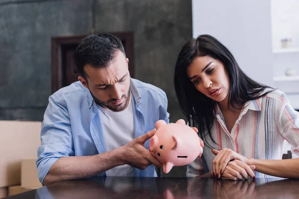 Concentrated man looking at piggy bank near woman with clenched hands at table — Stock Photo