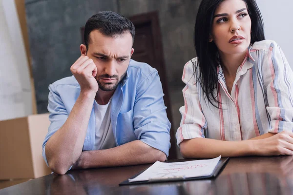 Konzentrierter Mann liest neben Frau Dokumente und blickt auf Tisch — Stockfoto