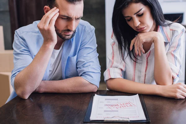 Uomo concentrato e teso che legge documenti vicino alla donna con gli occhi chiusi a tavola — Foto stock