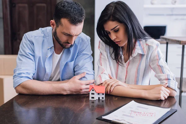 Verärgerte Bankrotteure schauen sich Hausmodell in der Nähe von Dokumenten am Tisch im Zimmer an — Stockfoto