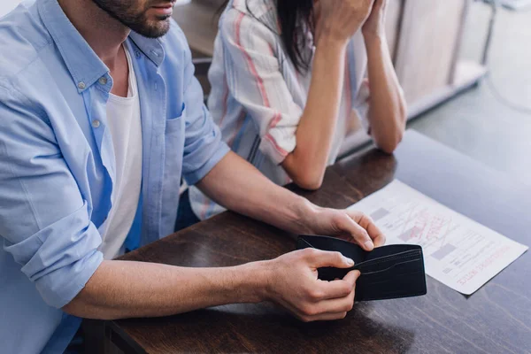 Cropped view of man holding empty purse near woman at table with document — Stock Photo