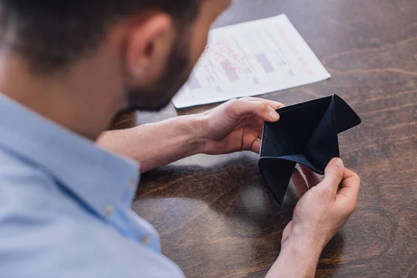 Cropped view of man looking at empty purse at table — Stock Photo