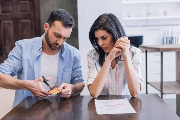 Uomo taglio carta di credito vicino alla donna con le mani serrate a tavola con documento in camera — Foto stock