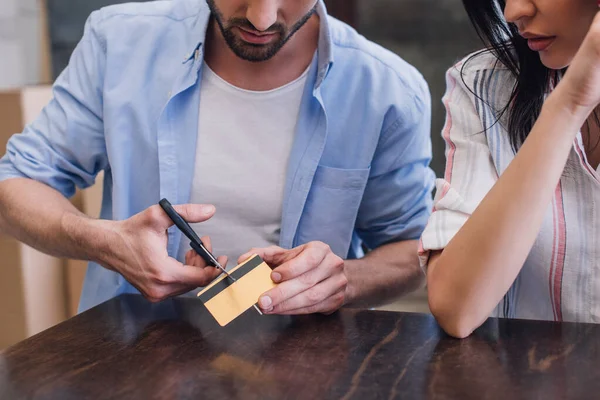 Обрезанный вид мужчины, разрезающего кредитную карту рядом с женщиной за столом — стоковое фото