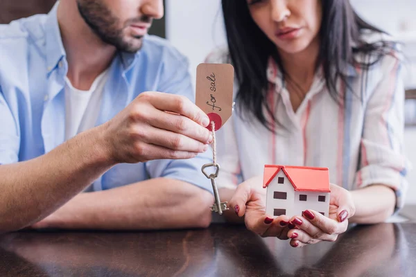 Cropped view of bankrupts showing key with for sale lettering and house model at table in room — Stock Photo