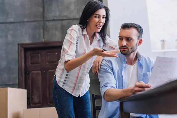 Stressed woman pointing at document in male hands at table in room — Stock Photo