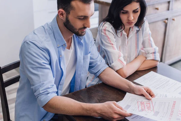 Vue en angle élevé de l'homme lisant le document avec forclusion et avis final lettrage près de la femme avec les bras croisés à la table — Photo de stock