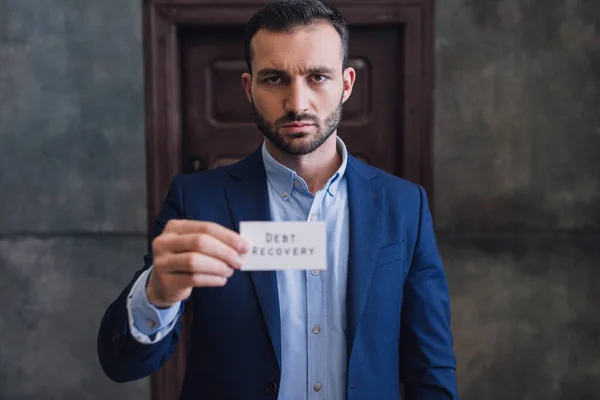 Enfoque selectivo del coleccionista mostrando tarjeta con letras de recuperación de deuda y mirando a la cámara - foto de stock