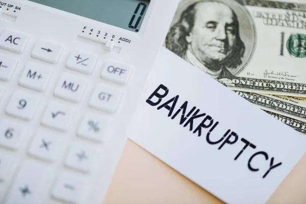 Top view of card with bankruptcy lettering, calculate and dollar banknotes on beige — Stock Photo