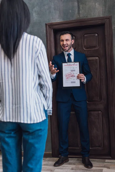 Angry collector with documents with foreclosure and final notice lettering shouting in front of woman in room — Stock Photo