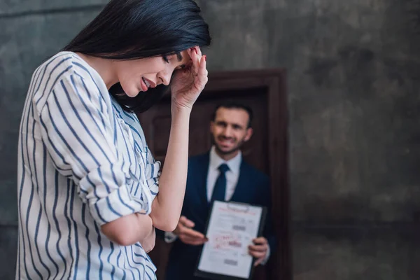 Selective focus of upset woman and angry collector with documents in room — Stock Photo