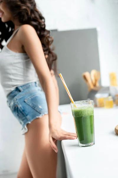 Selective focus of glass of smoothie on worktop and sexy woman in kitchen — Stock Photo