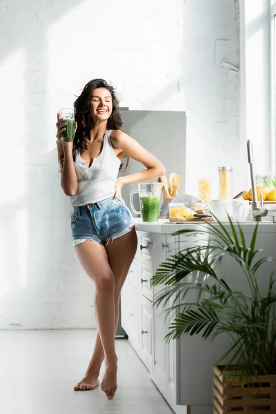 Focus selettivo della ragazza sorridente mentre tiene il bicchiere di frullato in cucina — Foto stock