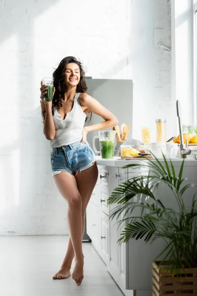 Selective focus of girl smiling while holding glass of smoothie in kitchen — Stock Photo