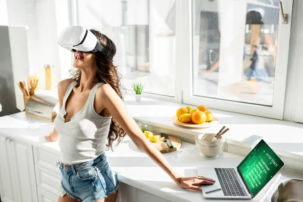 Woman using virtual reality headset near laptop and credit card in kitchen — Stock Photo