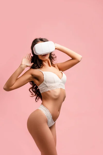 Vista lateral de chica sexy con las manos levantadas y auriculares de realidad virtual aislados en rosa - foto de stock