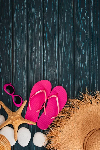 Draufsicht auf rosa Flip Flops in der Nähe von Sonnenbrille, Seestern und Meeressteinen auf dunklem Holzhintergrund — Stockfoto