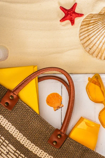 Top view of bag, sunscreen and book on white wooden planks near seashells on sand — Stock Photo