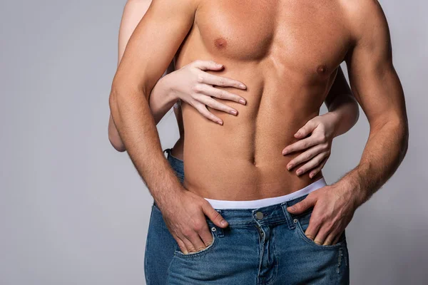 Corte vista de mulher tocando muscular namorado de pé com as mãos em bolsos isolados em cinza — Fotografia de Stock