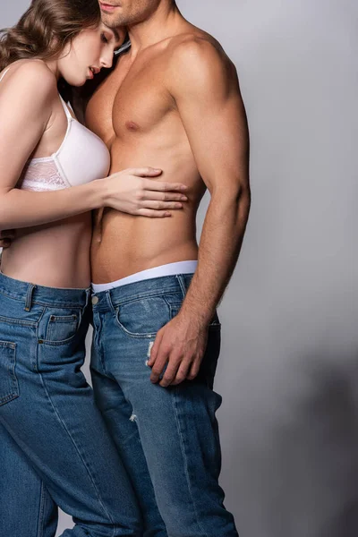 Приваблива дівчина обіймає м'язового чоловіка в джинсах на сірому — стокове фото