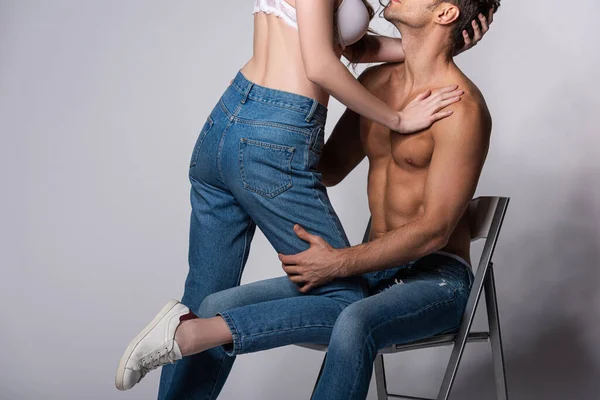Cropped view of seductive girl in bra touching muscular man sitting on grey — Stock Photo