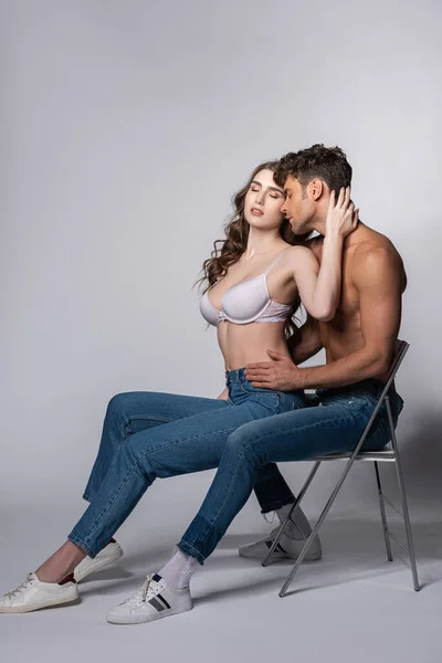 Seductive woman with closed eyes touching passionate man in jeans sitting on grey — Stock Photo