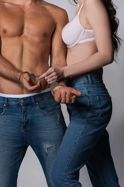 Vue recadrée de la femme dominante touchant les menottes sur l'homme musclé sur gris — Photo de stock