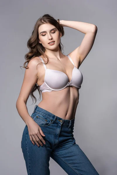 Seductive girl in bra and denim jeans standing isolated on grey — Stock Photo