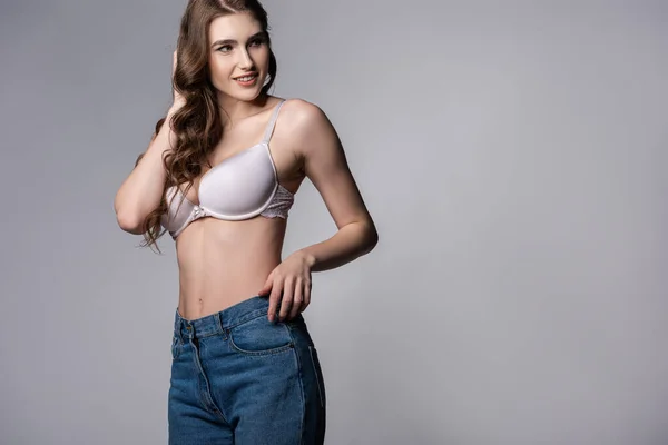Счастливая девушка в бюстгальтере и джинсах, стоящая на сером — стоковое фото