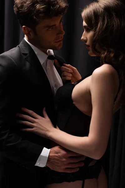 Donna seducente tirando cravatta di bell'uomo in tuta su nero — Foto stock