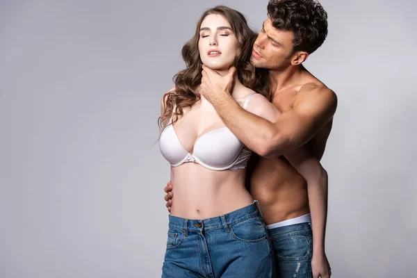 Uomo muscoloso in jeans toccare collo di ragazza in reggiseno bianco su grigio — Foto stock