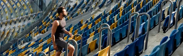 Young sportsman walking on stairs among seats at stadium, panoramic shot — Stock Photo