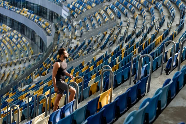 Young sportsman walking on stairs among seats at stadium — Stock Photo